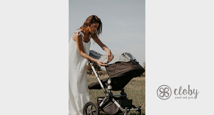 Mutter mit Kinderwagen beim befestigen einer UV-Decke am Kinderwagen mit dem cloby Magnetclip