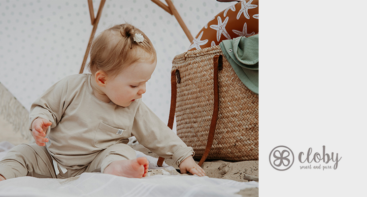 Kind mit beigefarbenem Longsleve von cloby sitzend am Strand