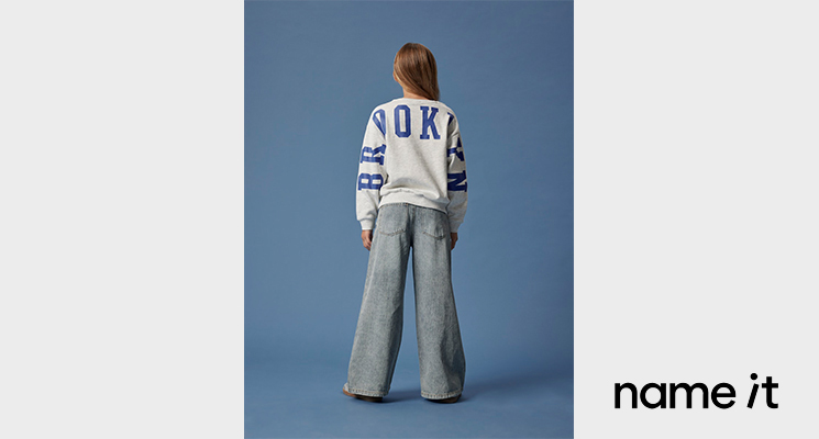 Mädchen mit Jeans und weißem Sweatshirt mit blauer Aufschrift von name it