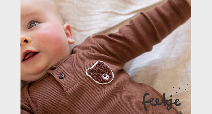 Baby mit braunem Oberteil mit Teddy-Aufnäher von feejte