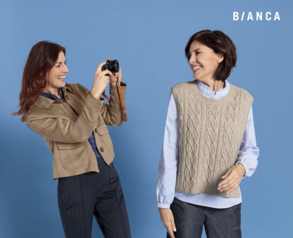 2 Frauen in Herbstmode. 1 Frau in Lederoptikjacke mit blauer Nadelstreifenhose, die andere Frau mit blauem Hemd, brauner Zopfmusterweste und blauer Jeans von Bianca