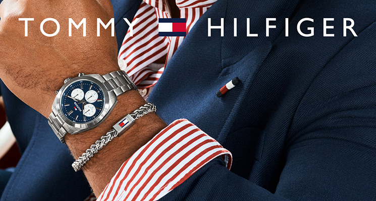 Herrenarm mit silberner Uhr und blauem Ziffernblatt. Armkettchen mit Tommi Hilfiger Logo