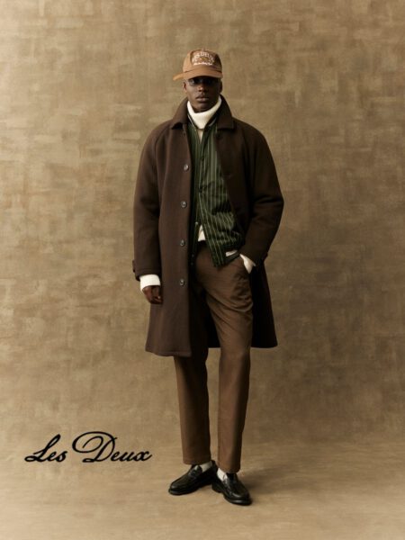 Mann mit brauner Hose, grün gestreiftem Hemd, braunem Mantel, weißer Rollkragenpullover und Cap von Les Deux