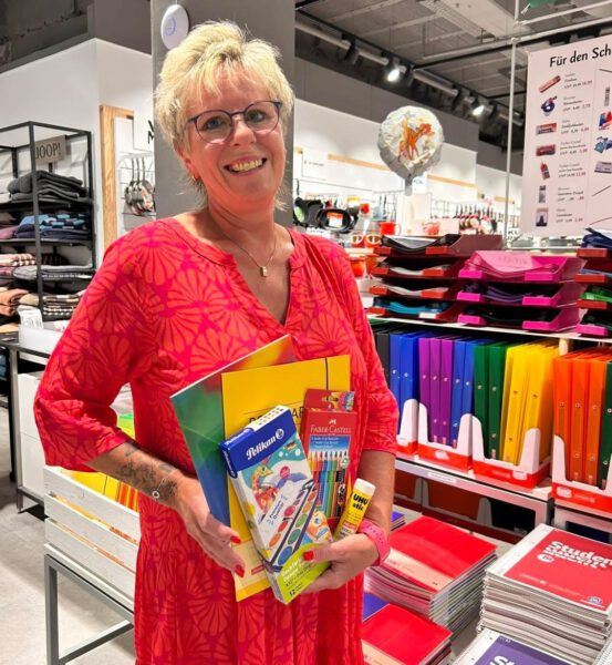Mitarbeiterin zeigt verschiedene Angebote zum Schulanfang wie z.B. Hefte, Stifte, Postmappe.