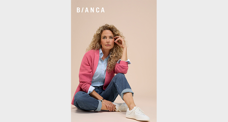 Model sitzend mit blauer Bluse, roséfarbenen Jäckchen und Jeans von Bianca