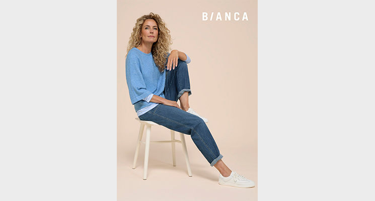 Model auf Stuhl sitzend mit blauem Pullover und blauer Jeans von Bianca