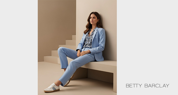 Frau auf Bank sitzend mit gemusterter Bluse, blauem Blazer und blauer Hose von Betty Barclay