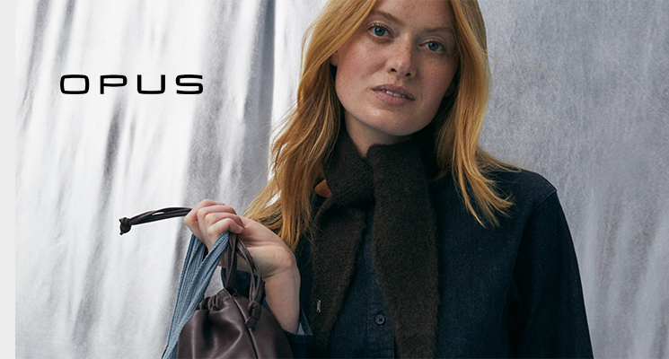 Frau mit dunkelblauem Hemd und Jeanshose, braunem Schal, brauner Handtasche und blauer Netztasche von Opus