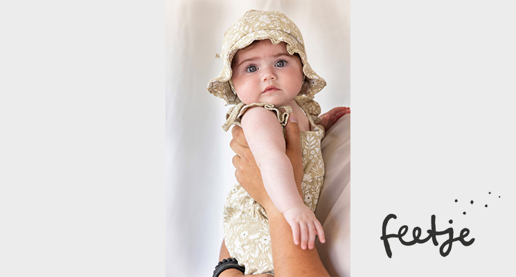 Baby Mädchen auf Arm mit khaki Sonnenmütze und khaki gemusterten Oberteil von Feetje