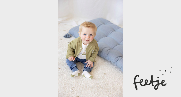 Kleiner Junge auf Boden sitzend mit khaki Jäckchen und Jeans von Feetje