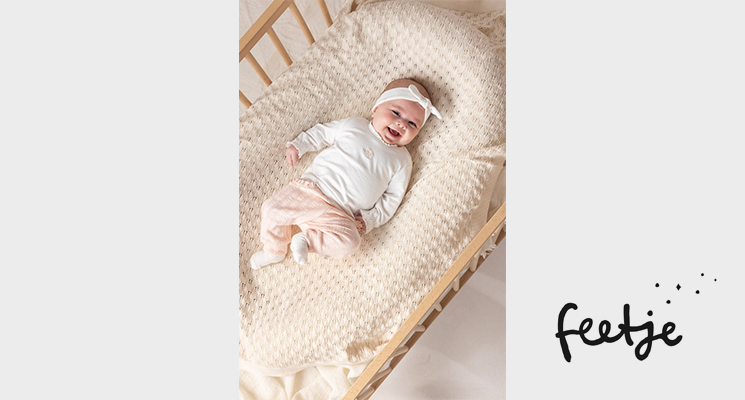Baby liegend in Bett mit weißem Langarmshirt und roséfarbener Hose und Haarband von Feetje