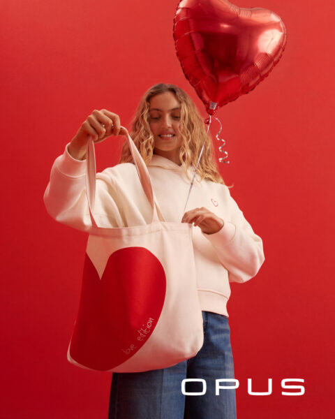Frau stehend mit Herztasche, weißem Hoodie mit Herz und blauer Jeans zum Valentinstag von Opus