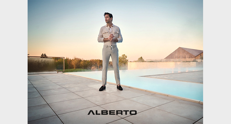 Mann in beigem T-Shirthemd und beiger Hose vor Pool stehend von Alberto