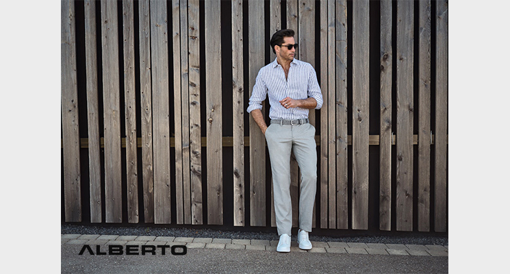 Mann in beige weiß gestreiftem Hemd mit beiger Hose und weißen Sneakern vor Bretterwand