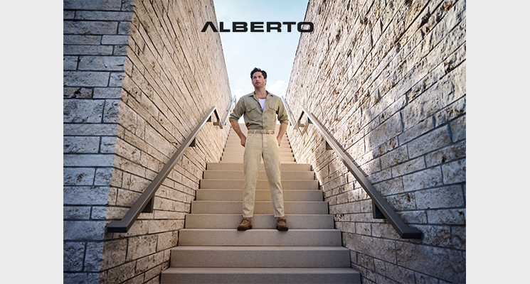 Mann auf Treppe stehend mit beigem leicht geöffnetem Hemd, darunter weißes T-Shirt und beiger Hose und braunen Halbschuhen