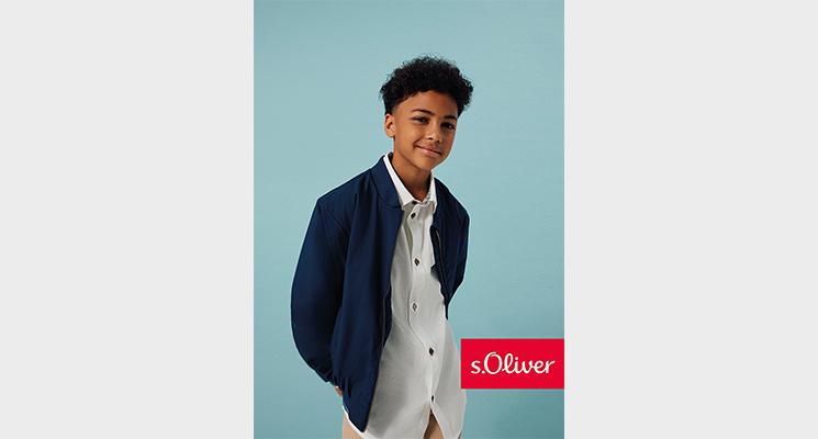 Junge mit verschränktem Armen hinter dem Rücken in weißem Hemd und blauer Blousonjacke von S.Oliver