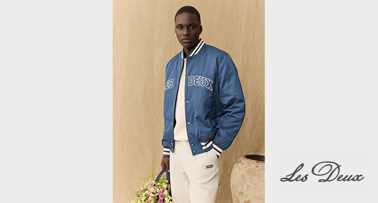 Mann in blauer Übergangsjacke und weißer Hose von Les Deux mit Blumenstrauß in der Hand