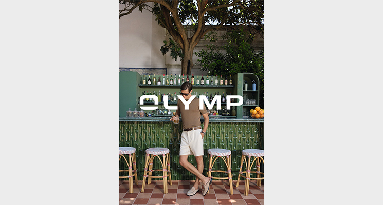 Mann stehend in Bar vor Barhockern in braunem Hemdshirt und weißer Hose von Olymp