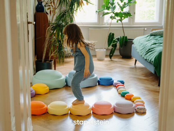 Stapelsteine in verschiedenen Farben und Größen wo Mädchen von Stein zu Stein hüpft