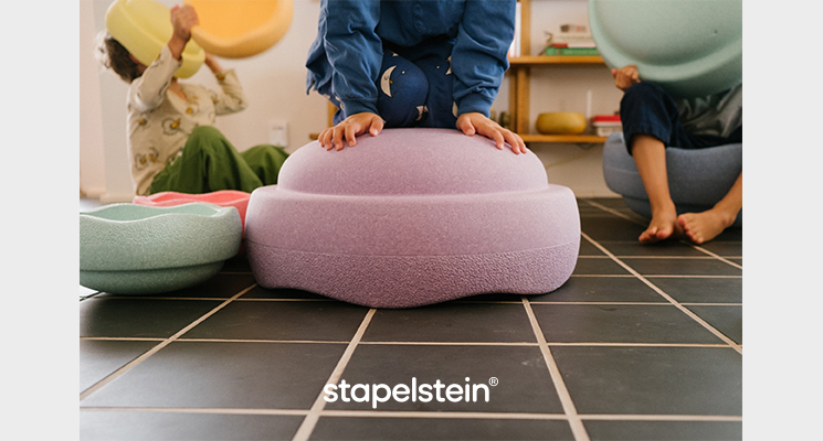 Kind kniet auf großem Stapelstein und andere Kinder spielen mit kleineren Stapelsteinen