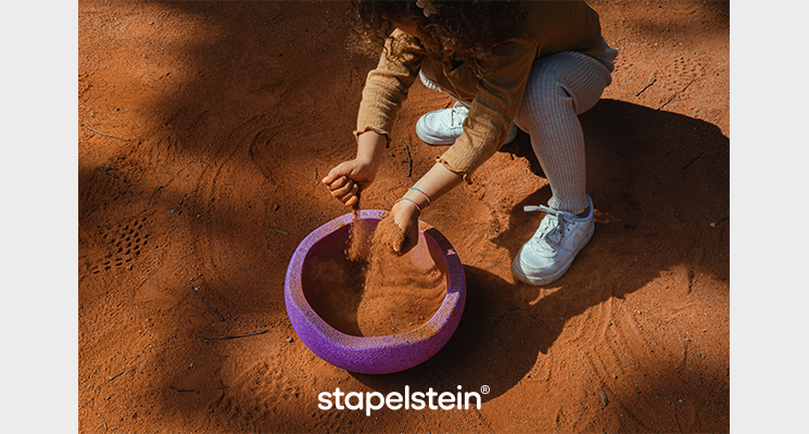 lilafarbener Stapelstein wird von Kind mit Sand zum Spielen befüllt