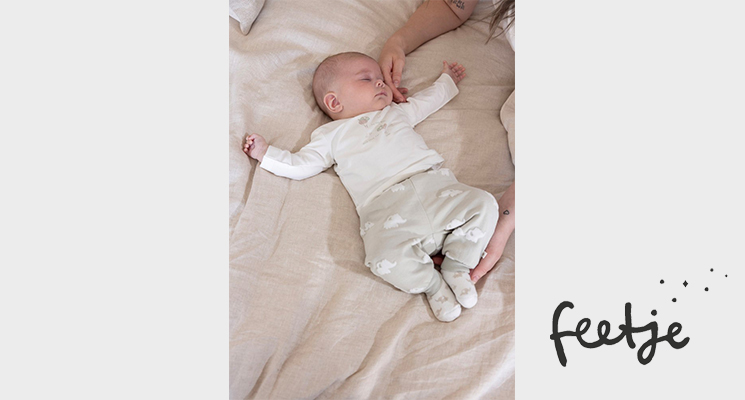 Baby in weißem Langarmshirt und beiger Hose auf Bett liegend von Feetje