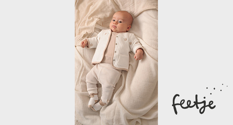 Baby auf Bett liegend in rosefarbenen Shirt, weißem Jäckchen und weißer Hose sowie Söckchen von Feejte