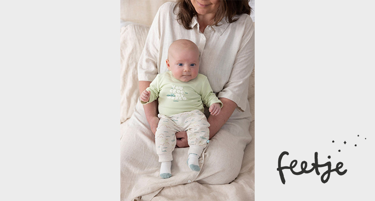 Mutter mit Baby im Arm welches mintgrünes Langarmshirt und weiße Hose und Söckchen trägt von Feetje