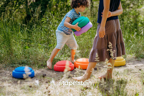 Mädchen und Junge spielen mit verschieden farbigen Stapelsteinen auf Wiesenweg