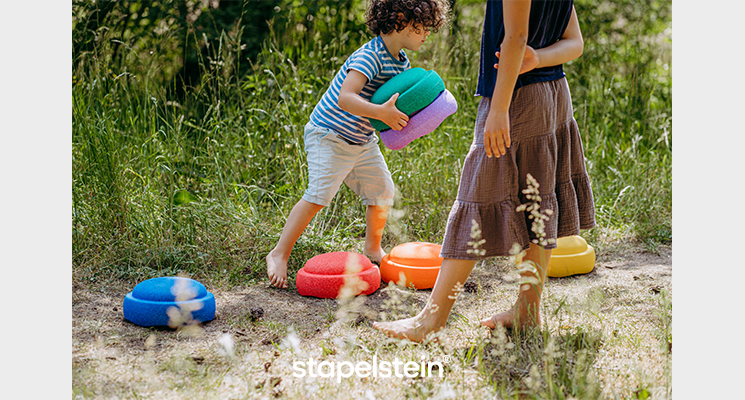 Mädchen und Junge spielen mit verschieden farbigen Stapelsteinen auf Wiesenweg