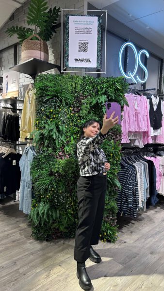 Mitarbeiterin vor grüner Selfie Wand im Erdgeschoss