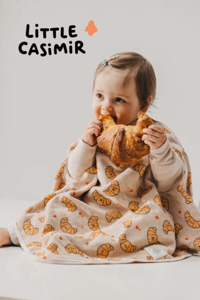 cremefarbener Latz mit Croissant Motiv an Kind welches auch Croissant isst von Little Casimir