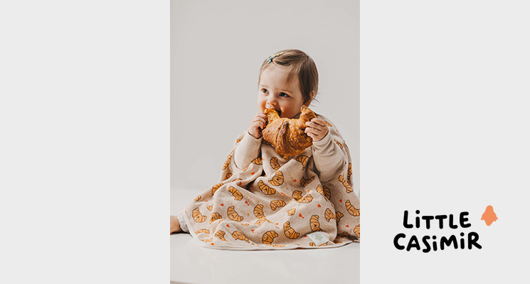 cremefarbener Latz mit Croissant Motiv an Kind welches auch Croissant isst von Little Casimir