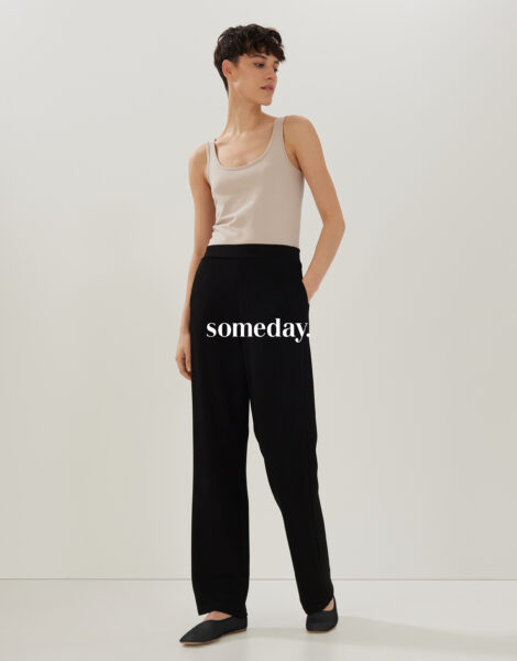 Stehende Fraumit beigem Top und schwarzer Hose von Someday