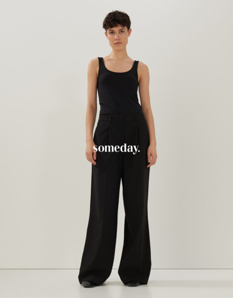Stehende Frau mit schwarzem Top und schwarzer Hose von Someday