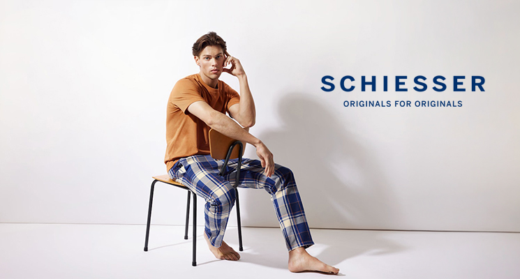 Sitzender Mann in Schlafanzug mit kurzem T-shirt in senfgelb und langer Hose in weiß blau kariert von Schiesser
