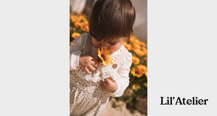 Kleines Mädchen auf Blumenwiese in weißem Langarmshirt und gemusterter Latzhose von Lil`Atelier