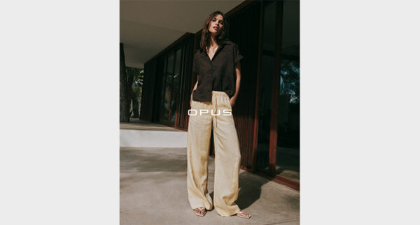Stehende Frau mit brauner Bluse und beiger Hose von Opus