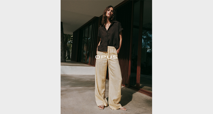 Stehende Frau mit brauner Bluse und beiger Hose von Opus