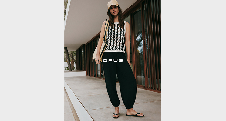Stehende Frau in weiß schwarzem Top und schwarzer Hose von Opus