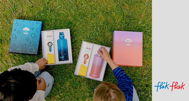2 Kinder von hinten. Mädchen und Junge mit jeweils einer Flik Flak Kinderuhr inklusive Sigg Trinkflasche in einer Geschenkbox für Geburtstag oder Einschulung