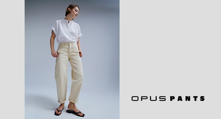 Stehende Frau in beiger OPUS PANTS und weißem Oberteil