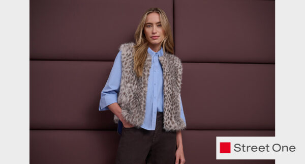 Stehende Frau mit hellblauer Bluse, gemusterter Teddyfellweste und brauner Hose von Street One
