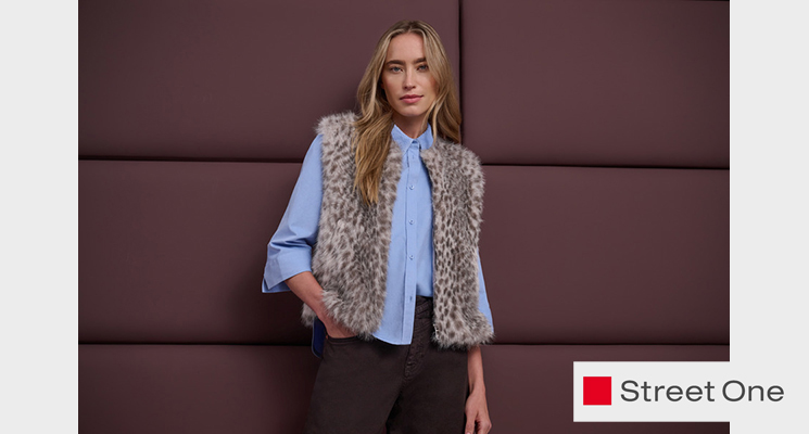 Stehende Frau mit hellblauer Bluse, gemusterter Teddyfellweste und brauner Hose von Street One