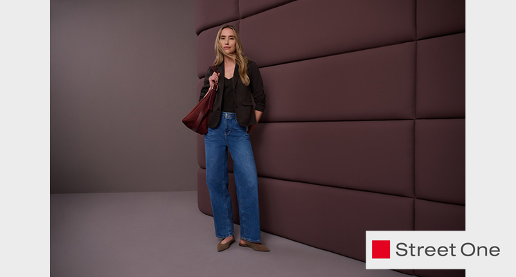 Stehende Frau mit schwarzer Jacke und Oberteil sowie blauer Jeans und bordeauxfarbener Tasche von Street One
