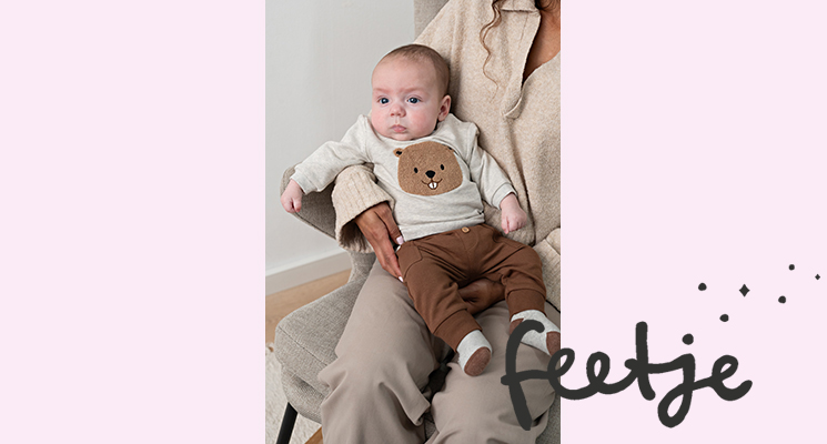 Baby Junge auf Frauenarm trägt beiges Langarmshirt mit Tieraufdruck und braune Hose von Feetje