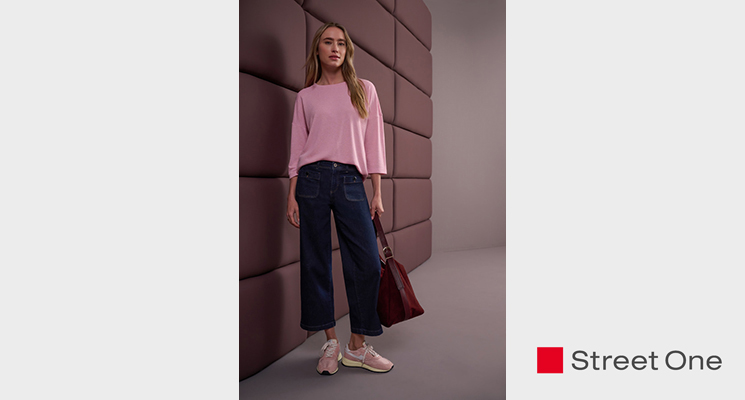 Stehende Frau mit rosafarbenem Langarmshirt, blauer Jeans und bordeauxfarbener Tasche von Street One