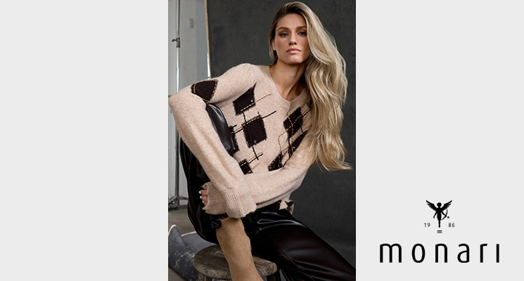Sitzende Frau trägt Pullover in beige mit schwarzen Farbblöcken und Strichen von Monari