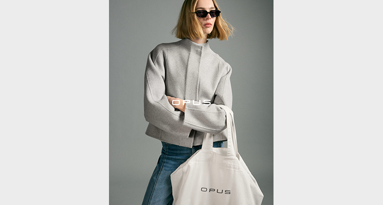 Frau mit Sonnenbrille in hellgrauer Jacke und blauer Jeans und Opus Stofftasche
