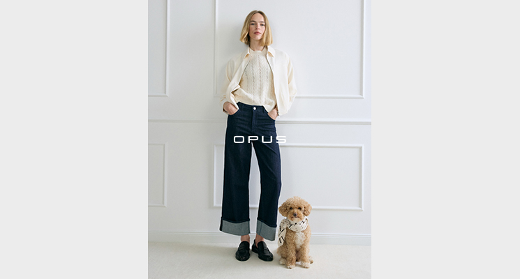 Stehende Frau in cremefarbenem Strickjäckchen, passendem Oberteil und blauer Jeans von Opus
